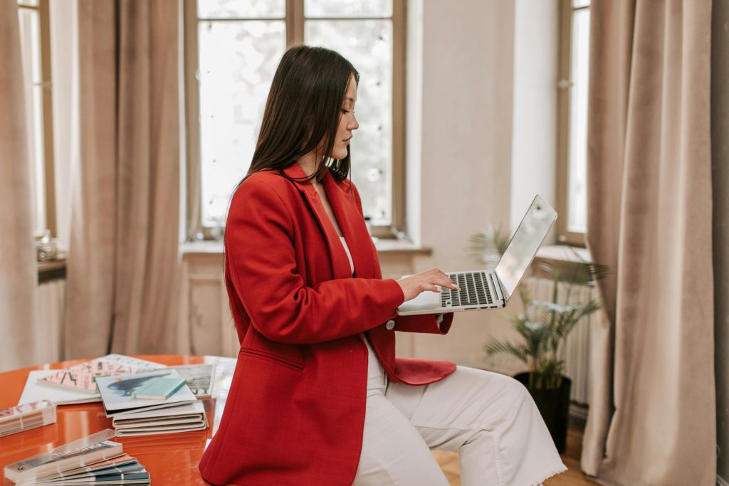 professional-looking woman sitting on the edge of a desk, holding a laptop in one hand